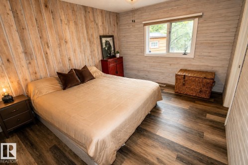 Spacious room featuring wood-finish flooring, two distinct wood-paneled accent walls, and a large window with white trim - 61 Stang Cres, Rural Two Hills County, AB 