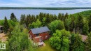 Red-sided residence featuring a dark gray roofline, surrounded by dense evergreen and deciduous trees, with a prominent body of water in the background - 61 Stang Cres, Rural Two Hills County, AB 