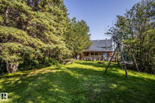 Expansive grassy lawn surrounded by mature trees, featuring a wooden picnic table and a rustic wooden swing set - 61 Stang Cres, Rural Two Hills County, AB - Outdoor