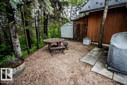 Gravel patio area featuring a wooden picnic table, flanked by mature trees and a wooden storage shed - 61 Stang Cres, Rural Two Hills County, AB - Outdoor