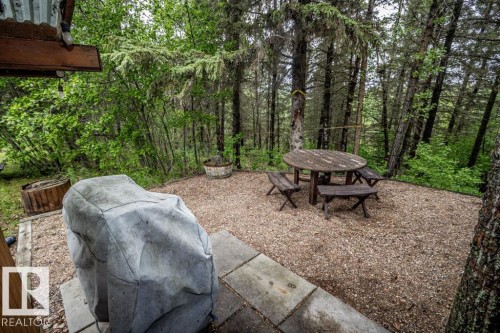 Gravel patio area featuring a round wood table with benches, surrounded by mature trees - 61 Stang Cres, Rural Two Hills County, AB - Outdoor
