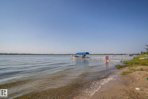 Waterfront setting featuring a sandy beach, calm water, a private dock system, and a pontoon boat - 61 Stang Cres, Rural Two Hills County, AB - Outdoor With Body Of Water With View