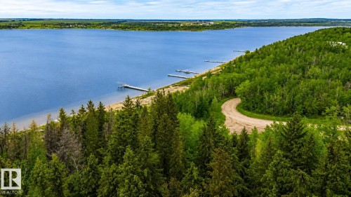 Expansive waterfront property featuring a sandy beach, multiple private docks, and mature evergreen and deciduous trees - 61 Stang Cres, Rural Two Hills County, AB - Outdoor With Body Of Water With View