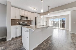 Kitchen featuring white cabinetry, stainless steel appliances, a large island with sink, dark subway tile backsplash, and wood-finish flooring - 