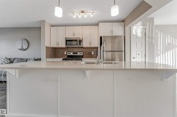 Kitchen island featuring a light-toned countertop, white cabinetry, stainless steel appliances, a tile backsplash, and overhead pendant lighting - 