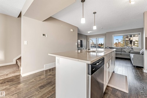 Kitchen island featuring a stainless steel dishwasher, an undermount sink with a high-arc faucet, and pendant lighting - 1624 33A Street, Edmonton, AB 