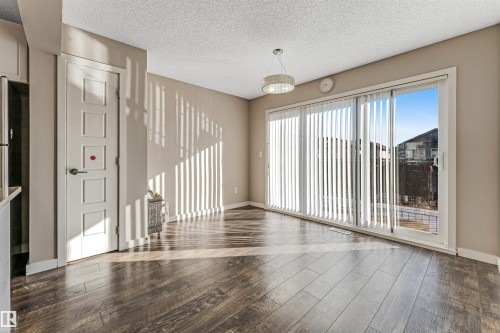 Spacious room featuring wood-finish flooring, a contemporary ceiling light fixture, and large sliding glass doors with vertical blinds - 1624 33A Street, Edmonton, AB 