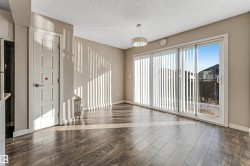 Spacious room featuring wood-finish flooring, a contemporary ceiling light fixture, and large sliding glass doors with vertical blinds - 
