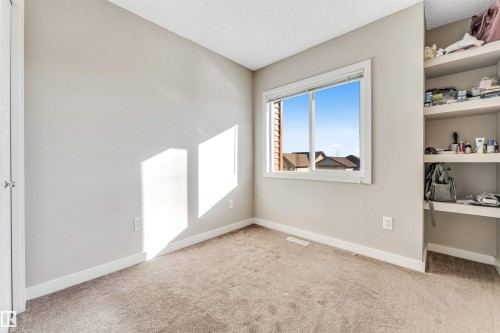 Neutral-toned room featuring a window with white trim, built-in shelving, light brown carpeting, and white baseboards - 1624 33A Street, Edmonton, AB 