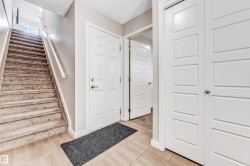Foyer featuring light-toned tile flooring, a carpeted staircase with white handrail, white paneled doors, and light neutral wall finishes - 