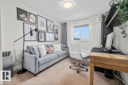 Carpeted room featuring a white window frame, white sheer curtains, and a built-in dark shelving unit - 