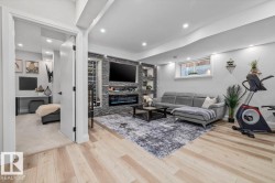 Finished lower level featuring a textured stone accent wall with an integrated electric fireplace, light wood-finish flooring and recessed lighting - 