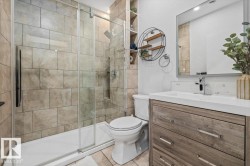 Bathroom featuring a glass-enclosed shower with full-height tile surround, a single vanity with wood-finish cabinetry, a white countertop, and a large wall-mounted mirror - 