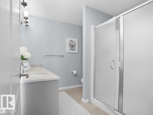 Bathroom featuring a double vanity with stone-look countertop, integrated sinks, chrome faucets, and a glass-enclosed shower with a sliding door - 207 41 Avenue, Edmonton, AB 