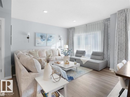Open-concept living area featuring light wood-finish flooring, recessed lighting, and a large window with sheer and patterned drapes - 207 41 Avenue, Edmonton, AB 