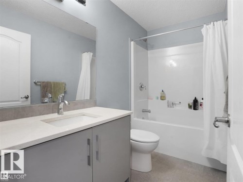 Bathroom featuring a single vanity with a light-colored countertop and a chrome faucet, a large mirror, a white bathtub with a shower kit, and light gray wall paint - 207 41 Avenue, Edmonton, AB 
