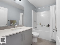 Bathroom featuring a single vanity with a light-colored countertop and a chrome faucet, a large mirror, a white bathtub with a shower kit, and light gray wall paint - 