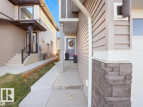 Front entryway featuring a grey door, concrete walkway, and stone-accented pillar - 207 41 Avenue, Edmonton, AB 