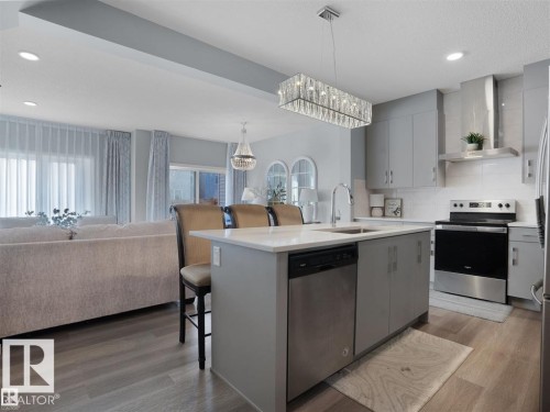 Contemporary kitchen featuring an island with a breakfast bar, stainless steel appliances, light gray cabinetry, a white subway tile backsplash, and wood-finish flooring - 207 41 Avenue, Edmonton, AB 