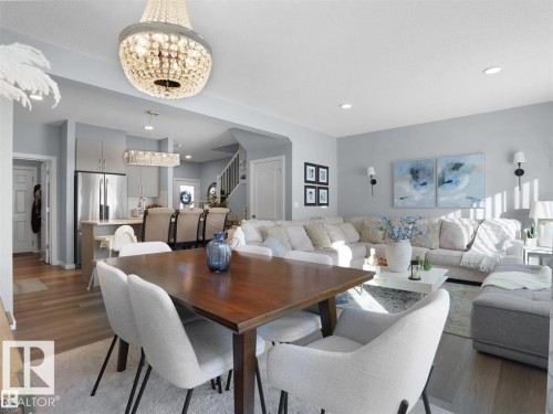 Open-concept living space featuring a crystal chandelier, wood-finish flooring, a kitchen with stainless steel appliances, a breakfast bar, and a staircase with dark railings - 207 41 Avenue, Edmonton, AB 