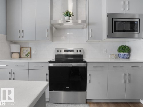 Modern kitchen featuring sleek gray cabinetry, stainless steel appliances, a built-in microwave, and a white subway tile backsplash - 207 41 Avenue, Edmonton, AB 