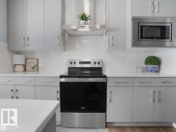 Modern kitchen featuring sleek gray cabinetry, stainless steel appliances, a built-in microwave, and a white subway tile backsplash - 