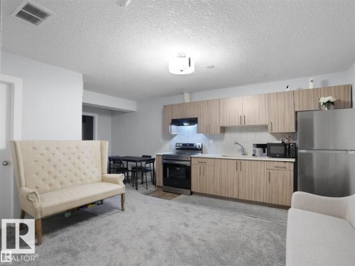 Open-concept living space with a kitchen featuring stainless steel appliances, wood-finish cabinetry, and light countertops - 207 41 Avenue, Edmonton, AB 