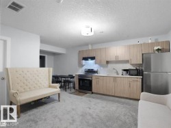 Open-concept living space with a kitchen featuring stainless steel appliances, wood-finish cabinetry, and light countertops - 
