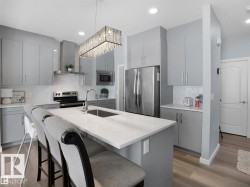 Modern kitchen featuring a central island with seating, light gray cabinetry, stainless steel appliances, white subway tile backsplash, and wood-finish flooring - 