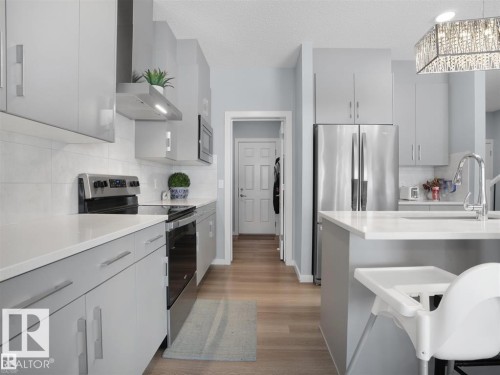 Contemporary kitchen featuring light gray cabinetry, stainless steel appliances, white countertops, a white subway tile backsplash, and wood-finish flooring - 207 41 Avenue, Edmonton, AB 