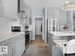 Contemporary kitchen featuring light gray cabinetry, stainless steel appliances, white countertops, a white subway tile backsplash, and wood-finish flooring - 