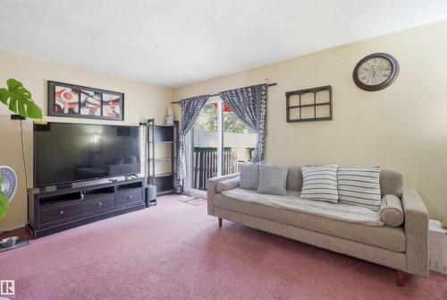 Living area featuring carpet flooring, light-toned walls, and a sliding glass door providing access to an outdoor space - 17 Lakewood Village, Edmonton, AB 