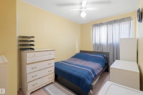 Bedroom featuring a ceiling fan with integrated lighting, a window with curtain rod, and light-toned walls - 17 Lakewood Village, Edmonton, AB 