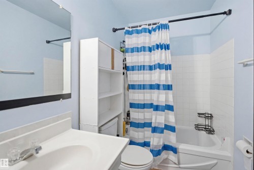 Bathroom featuring a full vanity with an integrated sink, a rectangular mirror, a built-in tub with white subway tile surround, and an open shelving storage unit - 17 Lakewood Village, Edmonton, AB 