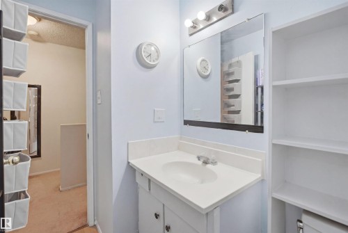 Bathroom vanity featuring a white countertop with an integrated sink, a large wall-mounted mirror, and a three-bulb vanity light fixture - 17 Lakewood Village, Edmonton, AB 