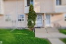 Exterior facade featuring a stucco finish, ground-level entry, and a mature evergreen shrub - 17 Lakewood Village, Edmonton, AB 