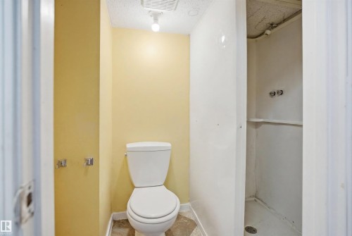 Bathroom featuring a floor-mounted toilet, light yellow painted walls, and a white shower stall with a built-in shelf - 17 Lakewood Village, Edmonton, AB 