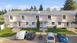 Multi-unit property featuring light-colored stucco exterior, individual entrances, and a gray shingle roof - 