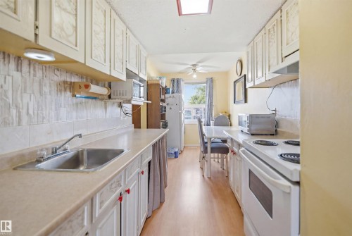 Galley kitchen featuring light-colored cabinetry, a stainless steel sink, a skylight, and wood-finish flooring - 17 Lakewood Village, Edmonton, AB 