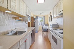 Galley kitchen featuring light-colored cabinetry, a stainless steel sink, a skylight, and wood-finish flooring - 
