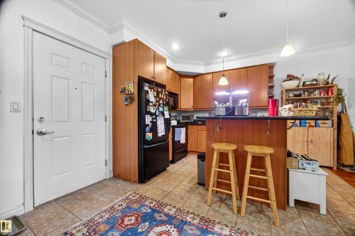 Functional kitchen featuring wood cabinetry, black appliances, a breakfast bar, and tile flooring - 304 10116 80 Avenue, Edmonton, AB 