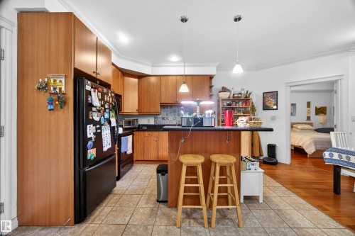 Kitchen featuring wood cabinetry, black appliances, a peninsula island with seating, and tile flooring - 304 10116 80 Avenue, Edmonton, AB 