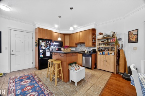 Open-concept kitchen featuring wood cabinetry, a breakfast bar with pendant lighting, a tile backsplash, and stainless steel appliances - 304 10116 80 Avenue, Edmonton, AB 