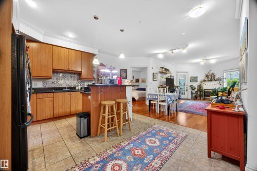 Kitchen featuring wood cabinetry, dark countertops, and a patterned tile backsplash - 304 10116 80 Avenue, Edmonton, AB 