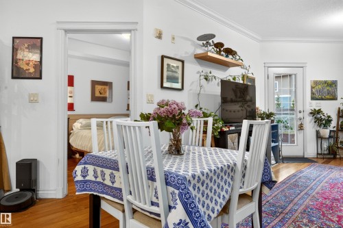 Hardwood flooring extends throughout the dining area and into the adjacent room, featuring white baseboards and crown molding - 304 10116 80 Avenue, Edmonton, AB 