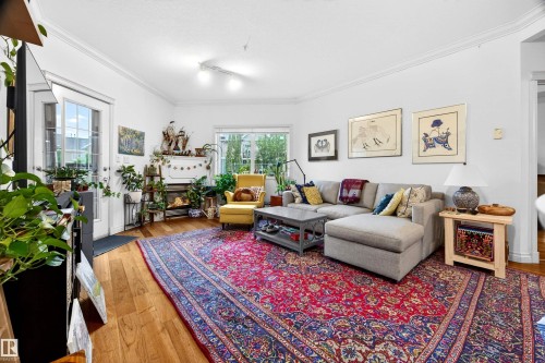 Bright living area featuring wood-finish flooring, white walls, crown molding, a large window, and a glass-paneled door - 304 10116 80 Avenue, Edmonton, AB 
