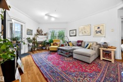 Bright living area featuring wood-finish flooring, white walls, crown molding, a large window, and a glass-paneled door - 