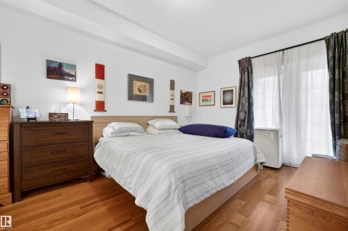 Bedroom featuring wood-finish flooring, a light wood bed frame, and white walls - 304 10116 80 Avenue, Edmonton, AB 