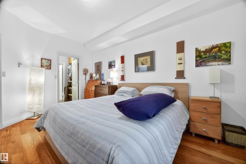 Bedroom featuring warm wood-finish flooring, white walls, and a light-colored wood headboard - 304 10116 80 Avenue, Edmonton, AB 
