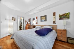 Bedroom featuring warm wood-finish flooring, white walls, and a light-colored wood headboard - 